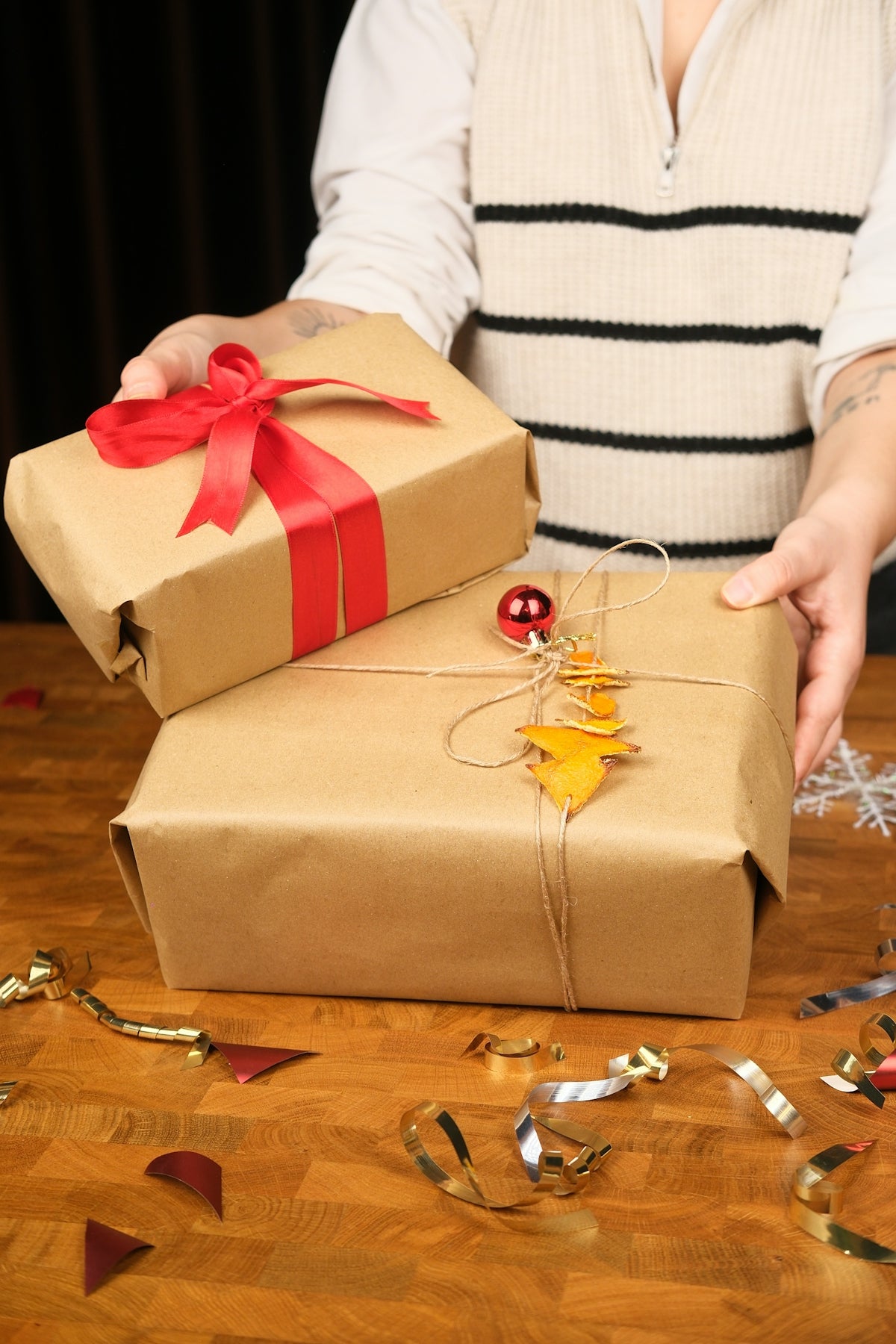 Hands holding two wrapped gifts with red ribbon.